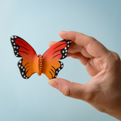 Hand holding a wooden butterfly toy against a blue background