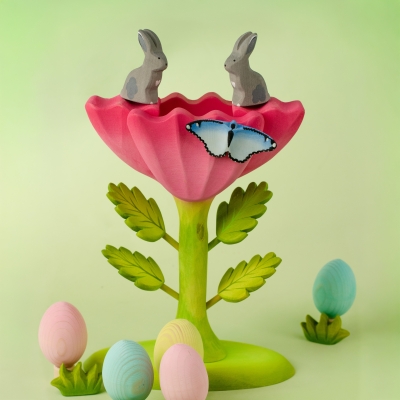 Child playing with wooden farm animals near a pink wooden Easter egg in a spring scene
