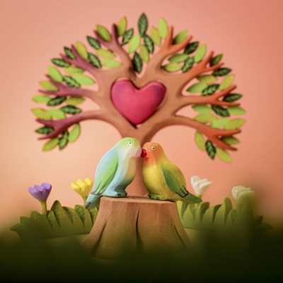 Two lovebirds, including the Green Lovebird, perched on a wooden stump in a whimsical nature scene with a heart-shaped tree.