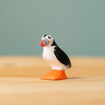 Front-side view of a wooden puffin toy showing the signature orange beak and black wings.