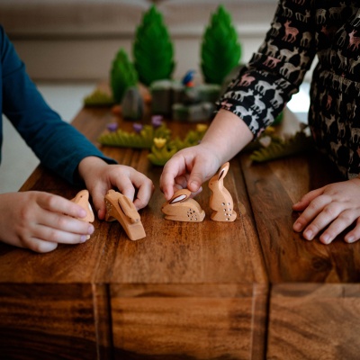 Pair of wooden rabbit toys, one slightly ahead of the other in a playful chase.