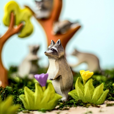 Handcrafted wooden raccoon toy standing among colorful flowers and trees by Bumbu Toys