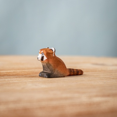 Handmade wooden red panda cub figure sitting on a wooden surface