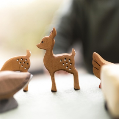 Child pushing the wooden fawn toy across a carpeted floor.