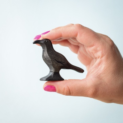 Hand holding a small handcrafted wooden raven figurine.