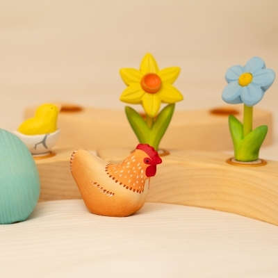 Hand-painted wooden toy hen and a yellow daffodil resting in a Waldorf celebration ring beside a blue daisy