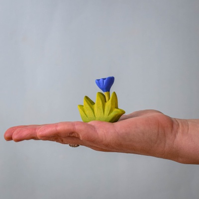 A small wooden grass and flower set held in hand, showcasing its size.