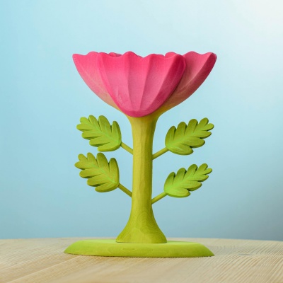 Identical wooden large pink flower with a green stem and leaves, photographed from the same angle on a wooden surface with a blue background.