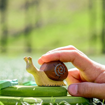 Child's hand holding a wooden snail toy outdoors