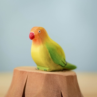 Green Lovebird wooden toy sitting on a wooden stump, hand-painted with vibrant eco-friendly colors.