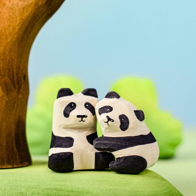 Two wooden panda bear cubs under a tree