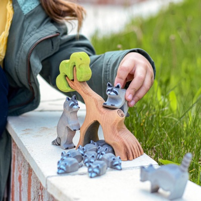 Child playing with a wooden raccoon family and tree toy set outdoors by Bumbu Toys