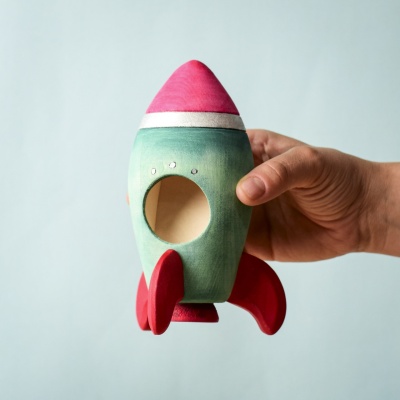 Hand holding the rocket, showcasing its round window and vibrant colors.