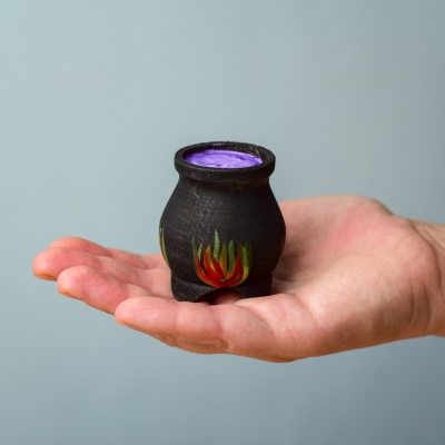 Hand holding a small handcrafted wooden cauldron with painted flames.