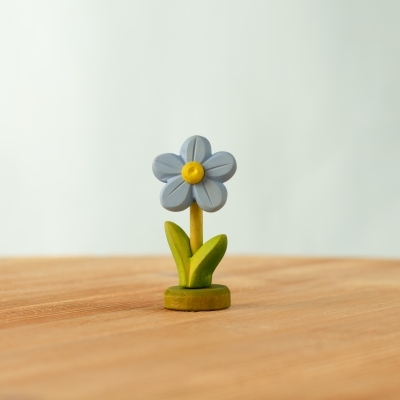 Two blue wooden flowers standing on green bases next to traditional dolls