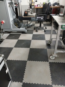 Radni prostor sa šahovskim podom od PVC ploča, opremljen mašinama, stolovima i stolicama.