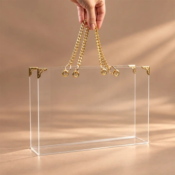 Geantă transparentă din plexiglas, ținută de mânerele din lanț metalic auriu
