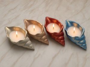 Smalti Sabbiati a base acqua: quattro portacandele a forma di conchiglia dipinti in oro champagne, oro rosa, oro rosso e oro azzurro con candele accese, accanto ai flaconi di smalto e vasi in gesso su piano in marmo. Prodotto disponibile su ConfettiPerfet