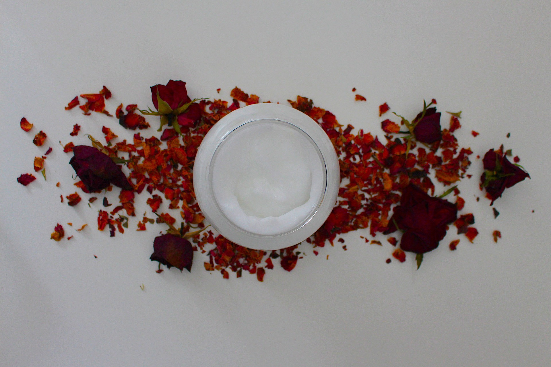 Recipient de crema de fata asezat pe petale de flori