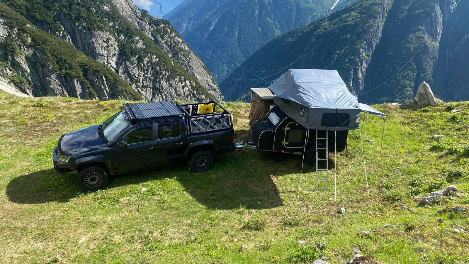 Pick-up cu rulotă teardrop și cort de plafon, pe o pajiște la munte