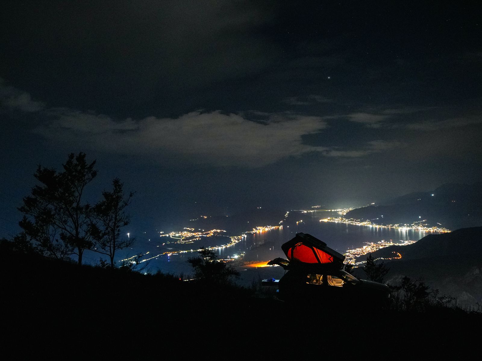 Golful Kotor noaptea, cu luminile de pe mal și un cort de acoperiș luminat în roșu în prim-plan