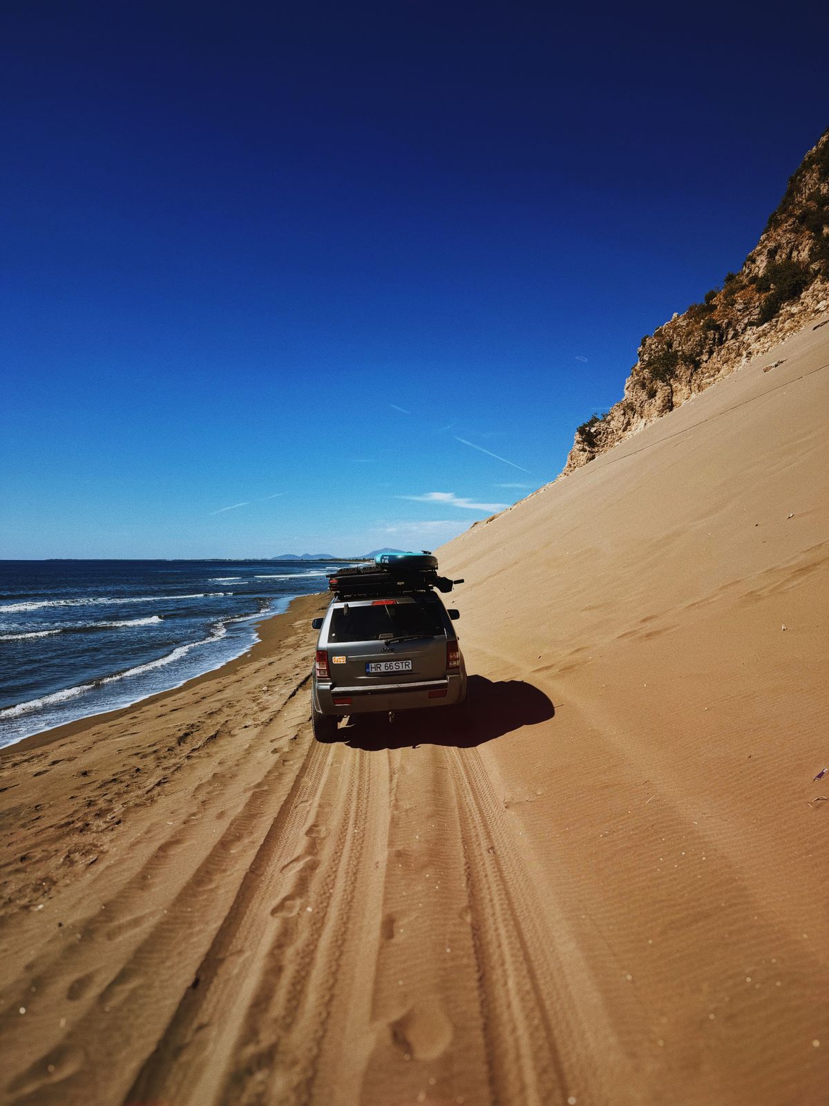 Un 4×4 pe plajă, lângă o pantă de nisip, cu marea în stânga