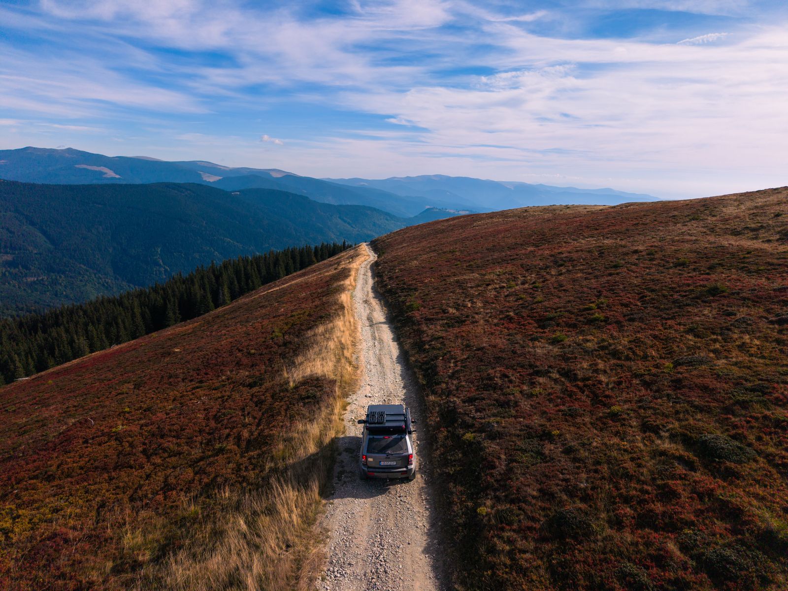 Vedere de sus a unui 4×4 pe un drum de munte printre pante cu iarbă roșiatică
