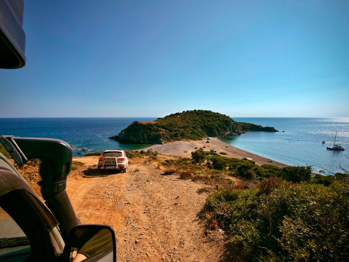 Vedere din Jimny spre un drum de pământ care coboară la o plajă și o peninsulă împădurită