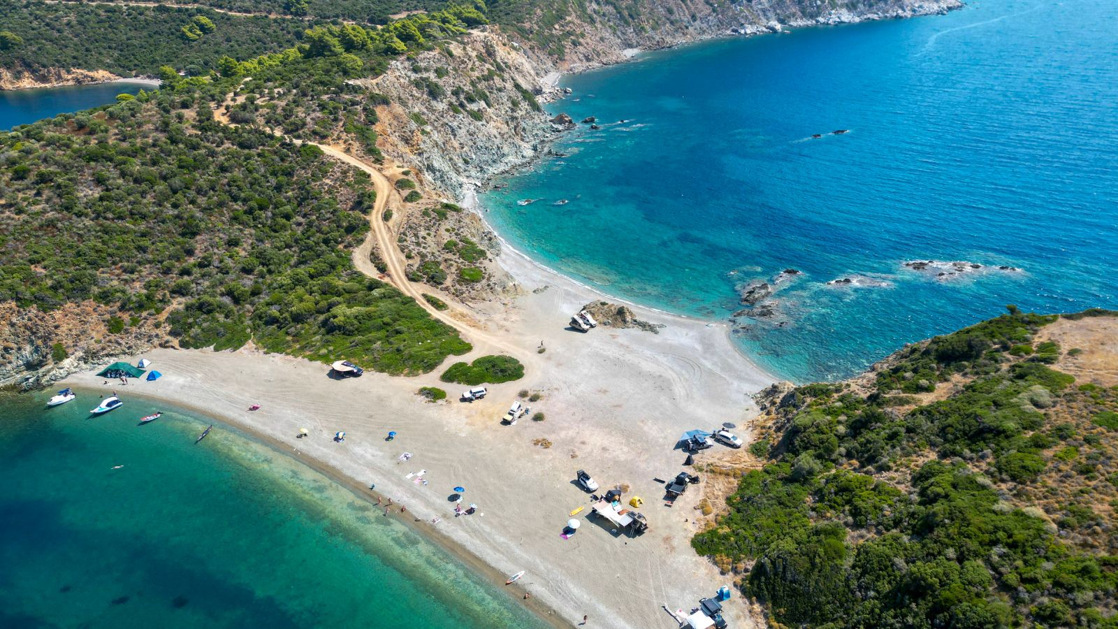 Imagine din dronă cu o plajă sălbatică între două golfuri, cu mașini și corturi de camping pe nisip