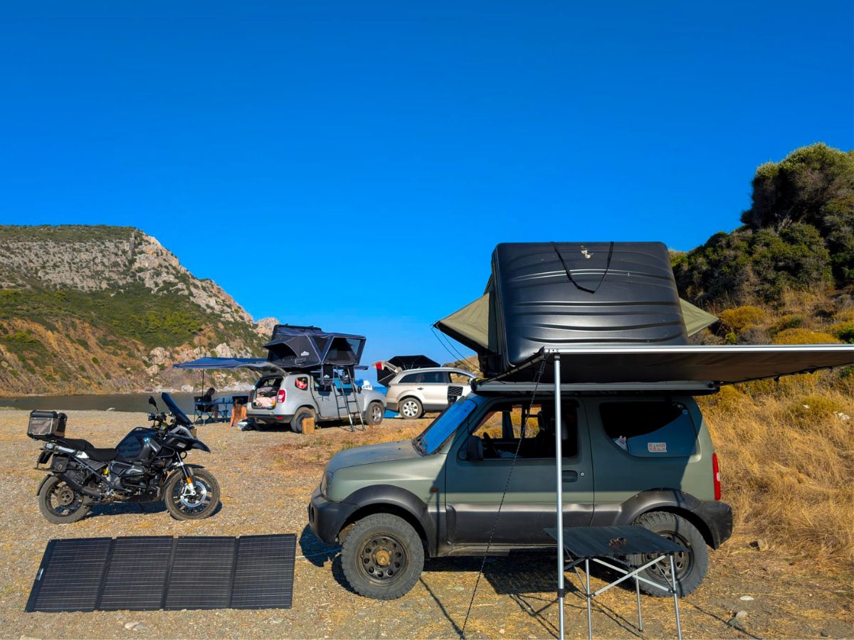 Tabără pe plajă: Suzuki Jimny cu cort de plafon și marchiză deschisă, o motocicletă și un panou solar