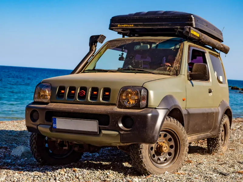 Suzuki Jimny cu cort de acoperiș închis, pe o plajă cu pietriș