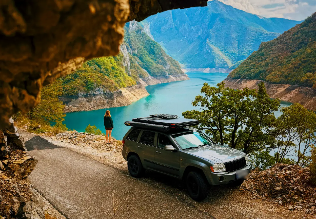 Mașină cu cort de acoperiș pe un drum de munte, deasupra unui lac