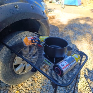 Aragazul portabil utilizat în camping, așezat pe o masă lângă o mașină 4x4.