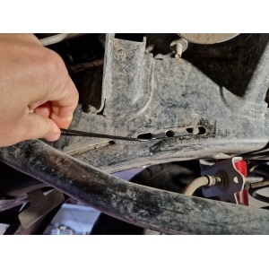 Mână indicând un punct de fixare pe șasiul unui Jeep Wrangler JL (2018+) pentru scutul motor.