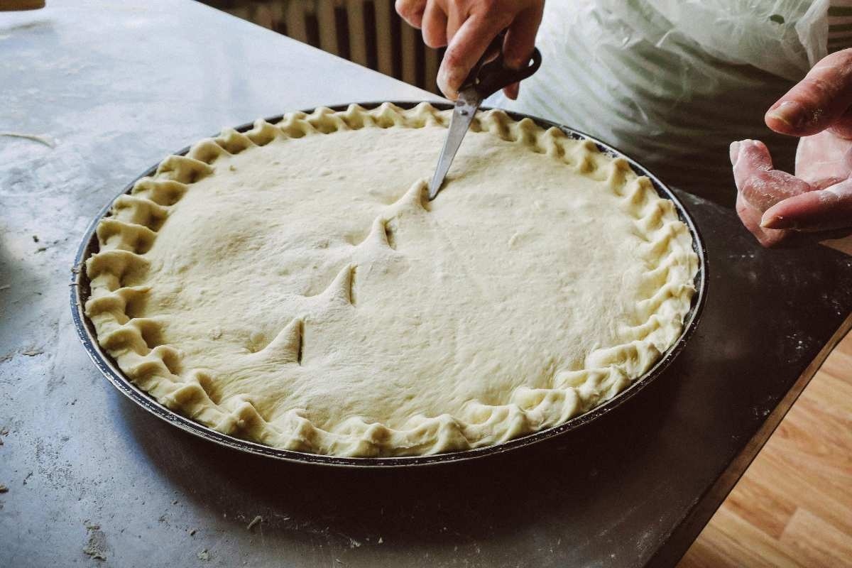 Coacerea blatului tartei cu caise – tehnici si sfaturi_Blat copt, persoana care pregateste blatul pentru tarta cu caise, tava de copt, masa