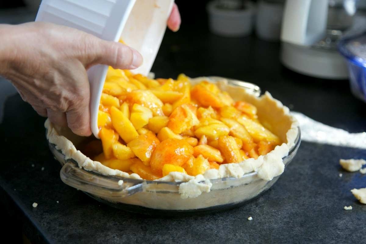 Reteta umpluturii cu caise a tartei – echilibru intre dulce si acrisor_Persoana adaugand caise in aluatul de tarta, ingrediente, vase, masa