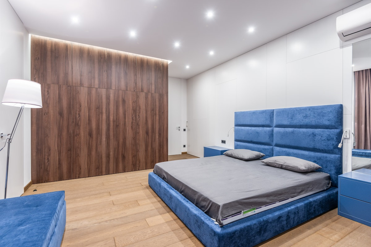Dormitor albastru - pat albastru, perete cu lemn in camera, camera mare si spatioasa, comoda in fata patului, lampa