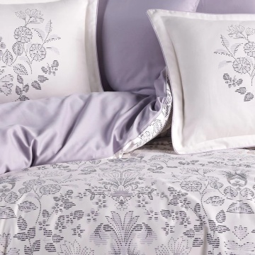 Detaliu lenjerie de pat din saten bumbac cu pilotă florală gri pe fundal alb și fețe de pernă albe cu imprimeu floral