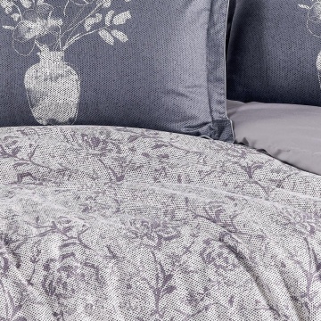 Detaliu lenjerie de pat din saten bumbac cu pilotă cu imprimeu floral în tonuri de gri și fețe de pernă gri cu vază albă