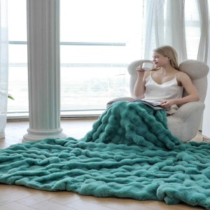 femeie asezata pe fotoliu si invelita in patura pufoasa turquoise din blanita artificiala