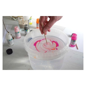 Vopsea Magic Marble Love Neon picurată pe apă, modelul tras cu un bețișor într-un vas metalic