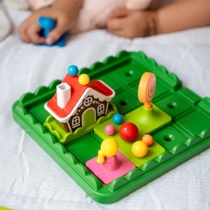 Joc de logică Hansel & Gretel de la Smart Games cu tablă de joc, figurine, case și piese de drum utilizate pentru rezolvarea celor 60 de provocări inspirate din basmul clasic.