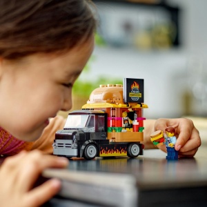 Tonetă mobilă LEGO City cu burger uriaș, camionetă și minifigurine vânzător și client, pregătită pentru aventuri culinare și jocuri de rol creative.