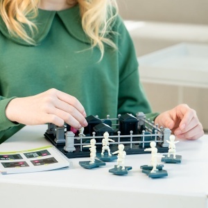 Joc de logică Smart Games Graveyard Shift cu tablă de joc, piese reprezentând scheleți și morminte, plus personaj și pisică într-un puzzle de evadare din cimitir.