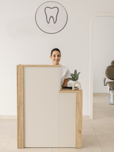 O recepționeră în spatele biroului, sub sigla unei clinici dentare