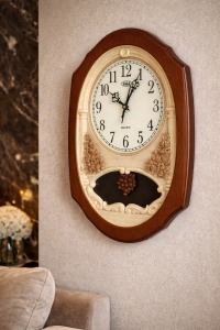 Ceas de perete clasic cu cadran rotund, cifre arabe mari și ornamente decorative în relief