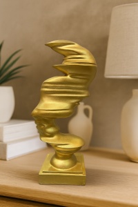 Statuetă decorativă aurie cu forme fluide, reprezentare abstractă a unei fețe stilizate