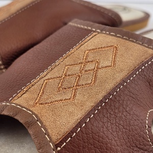 Detaliu premium cu broderia geometrică în formă de romburi aplicată fin pe pielea rezistentă de culoare maro.