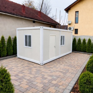Container alb în curte pavată, cu ușă centrală și ferestre prevăzute cu grilaje
