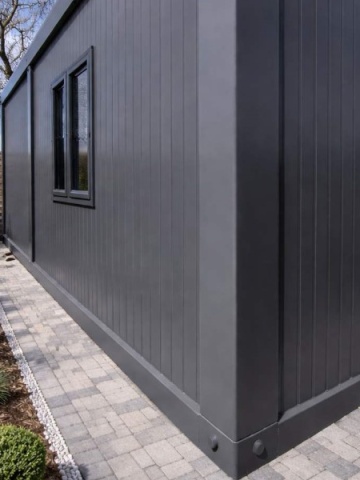Container depozitare sau birou exterior, amplasat pe alee pavată într-o grădină amenajată.